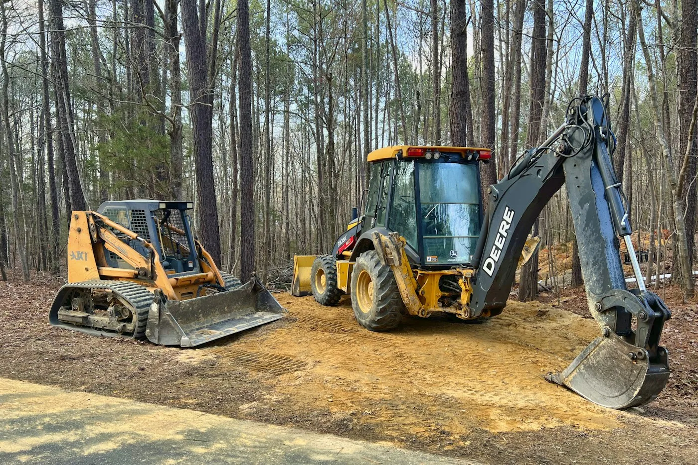 Excavator and backhoe loader in a wooded work area